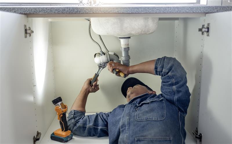 Plumber repairing pipes beneath a bathroom sink in Valrico
