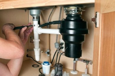 Plumber repairing a garbage disposal beneath a kitchen sink in Valrico