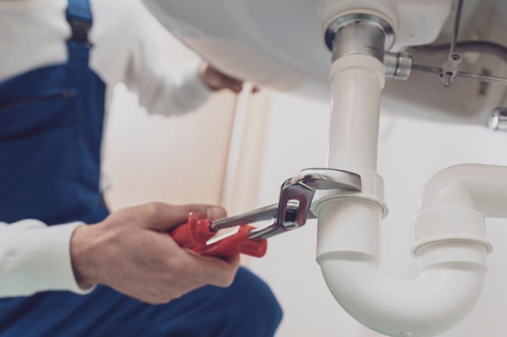 Plumber repairing a white drain pipe beneath a sink in Valrico